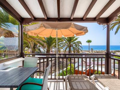 Balkon met tafel, zonnescherm en uitzicht op palmbomen en zee.