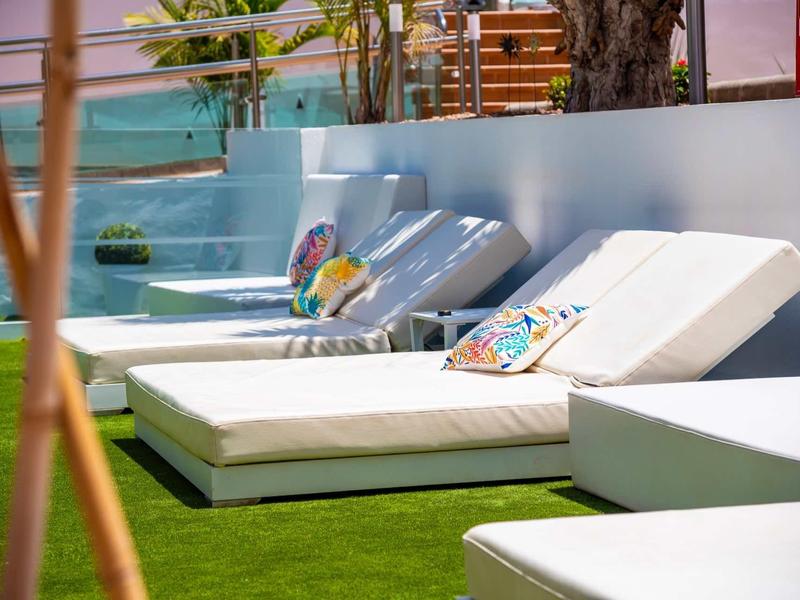 Witte ligstoelen met kleurrijke kussens op groen gras naast een zwembadgedeelte.