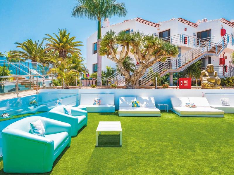 Moderne buitenzitplaatsen met blauwe fauteuils en witte banken op groen gras voor een hotel.