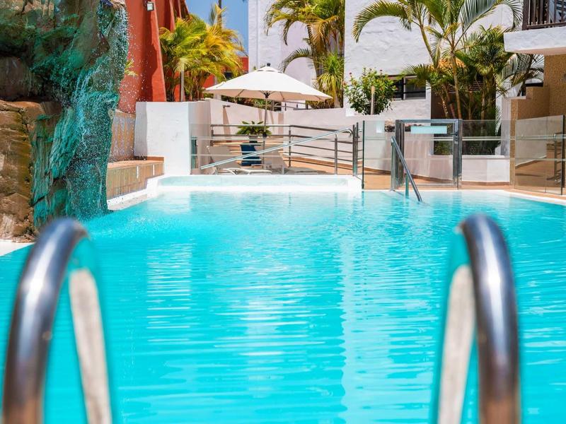 Helderblauw zwembad met metalen leuning en tropische planten op de achtergrond.