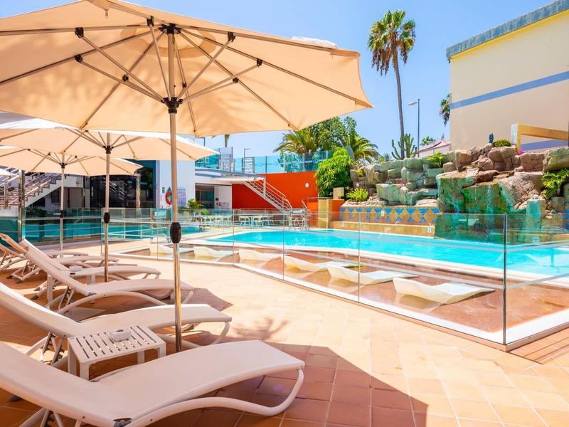 Zonnig zwembadgebied met ligstoelen, parasols en tropische planten.