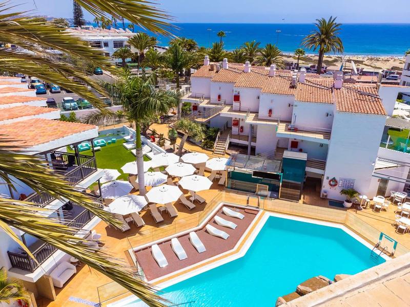 Hotel met buitenzwembad, ligstoelen en uitzicht op het strand en de zee.
