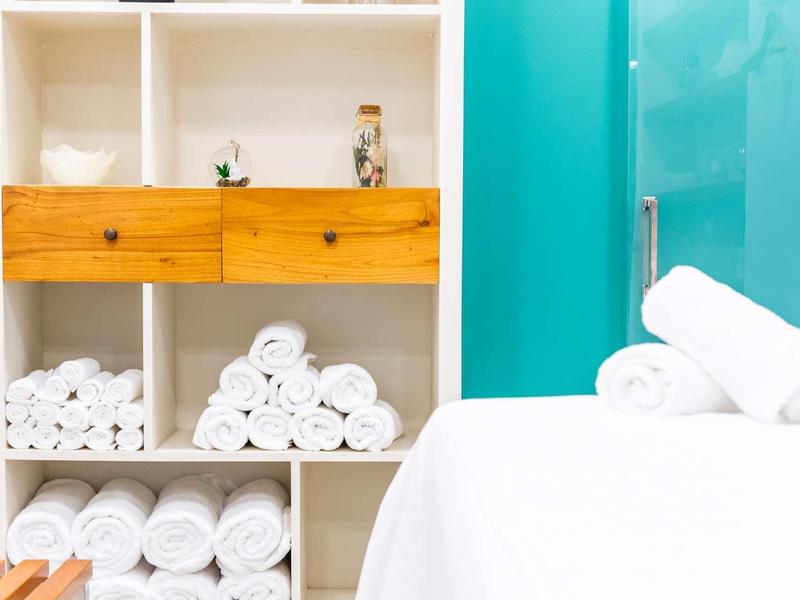 Witte handdoekstapels en houten meubels tegen een turquoise muur in een spa- of hotelkamer.