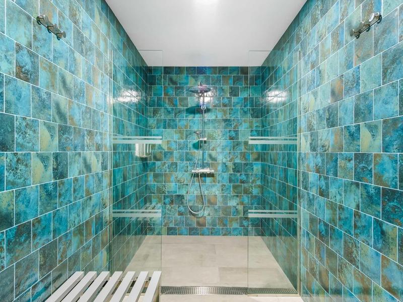 Grote douche met blauwgroene tegels en witte planken, modern en schoon.