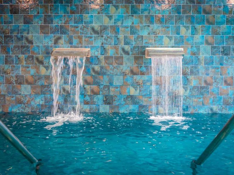 Twee watervallen stromen in een zwembad met turquoise tegels op de achtergrond.