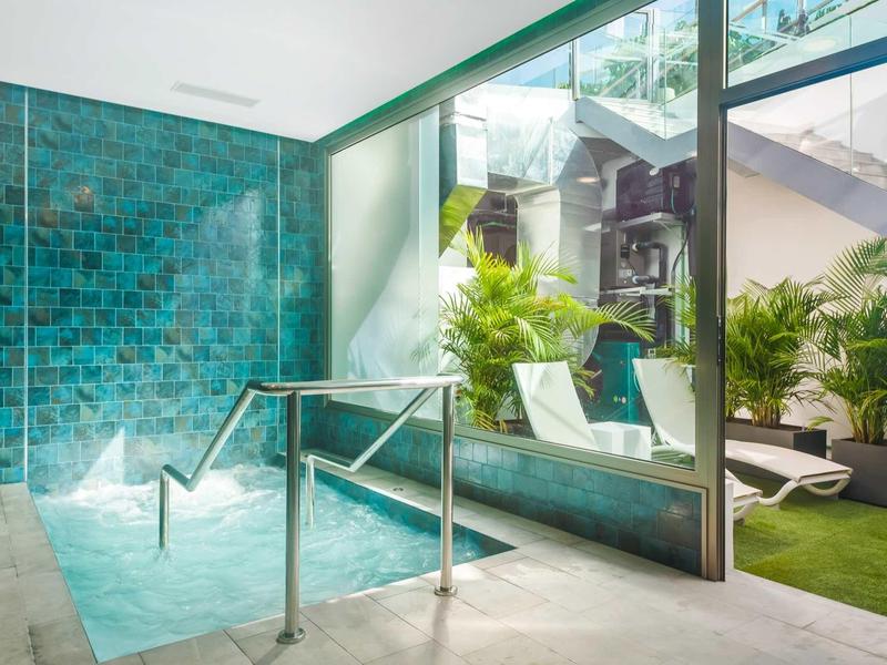 Moderne wellnessruimte met bubbelbad, glazen deur en ligstoelen naast een groen grasveld.