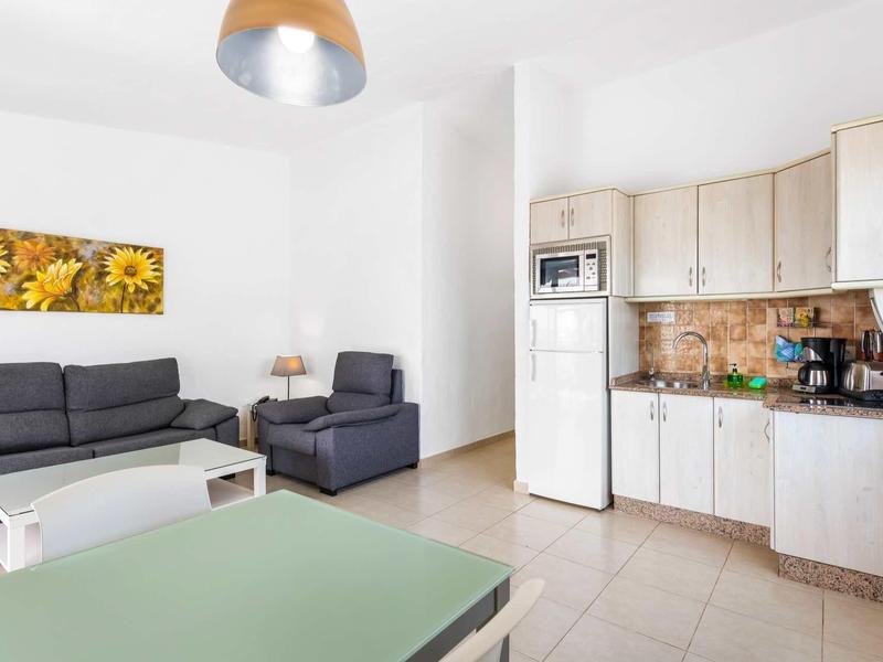 Lichte keuken en woonkamer met grijze bank en houten meubels in een vakantieappartement.