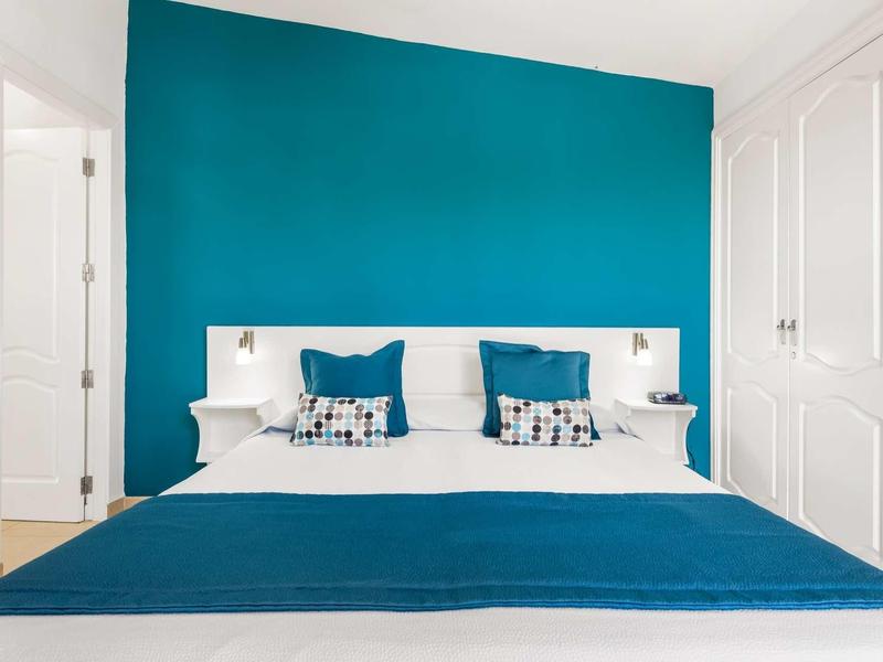 Moderne hotelkamer met tweepersoonsbed, turquoise muur en witte meubels.