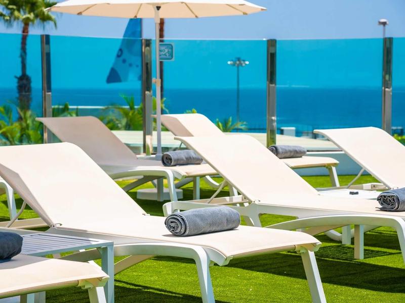 Witte ligstoelen met grijze handdoeken op gras bij glazen hek en zee