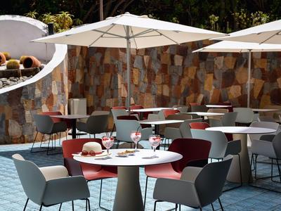 Area esterna moderna con tavoli, sedie e ombrelloni davanti a un muro di pietra.