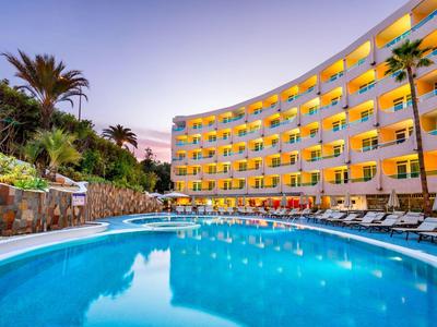 Zakład hotelowy o zakrzywionym kształcie z żółtymi balkonami nad okrągłym basenem o zachodzie słońca.