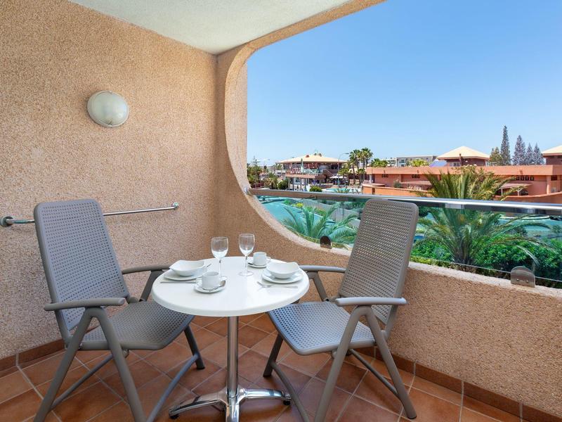 Przytulny balkon z dwoma krzesłami i stolikiem na kawę z widokiem na słoneczny kurort.