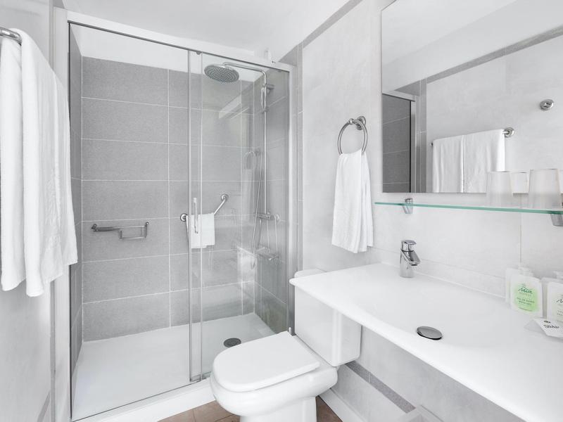 Jasna, nowoczesna łazienka z przeszklonym prysznicem, białymi ręcznikami, toaletą i dużym lustrem.