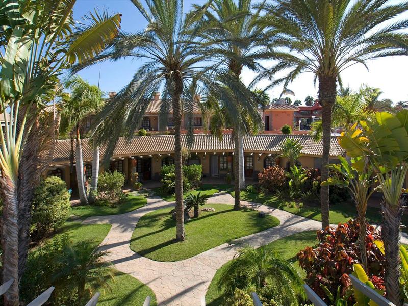 Giardino dell'hotel con palme, prati e sentieri curvi sotto il sole.