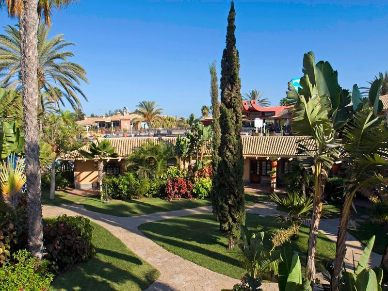 Edificio dell'hotel circondato da rigogliosi giardini tropicali e sentieri lastricati sotto un cielo azzurro.