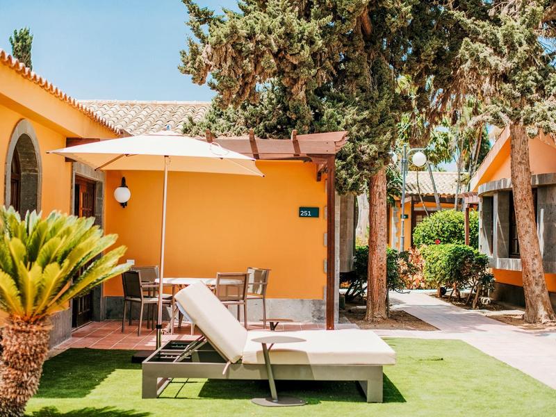 Sdraio confortevoli con ombrellone davanti a bungalow arancioni e alberi.