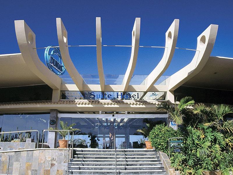 Bar all'aperto con bancone in legno e sedie bianche sotto un tetto aperto.