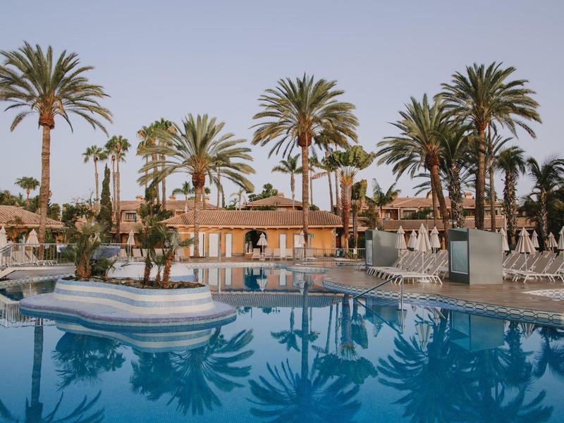 Grande piscina con lettini e palme in un resort alberghiero al tramonto.