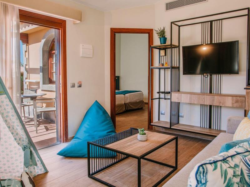 Soggiorno accogliente con divano, TV, cuscino blu e accesso al balcone.