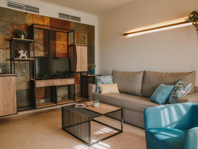 Area soggiorno accogliente in hotel con divano, poltrona e TV su parete elegante.