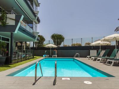 Piscine extérieure moderne à côté d'un hôtel avec chaises longues et parasols sous un ciel dégagé.