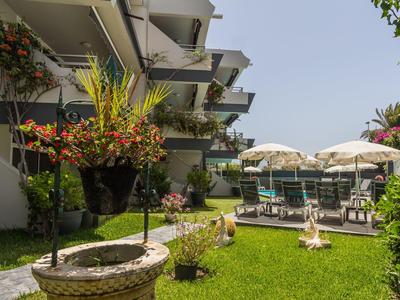 Giardino verde dell'hotel con sedie, ombrelloni e fiori accanto a un edificio moderno.