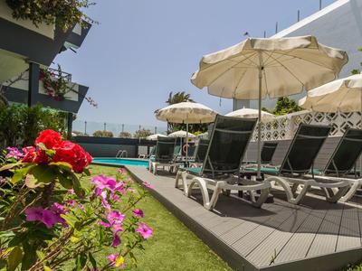 Transats avec parasols blancs à côté d'une piscine dans un hôtel avec des fleurs au premier plan.
