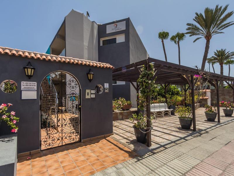 Entrée d'un hôtel avec portail, clôture peinte en violet, pergola et palmiers