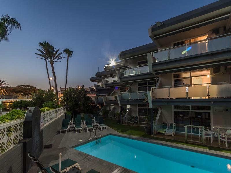 Espace piscine d'hôtel moderne avec piscine éclairée et chambres avec balcon au crépuscule.