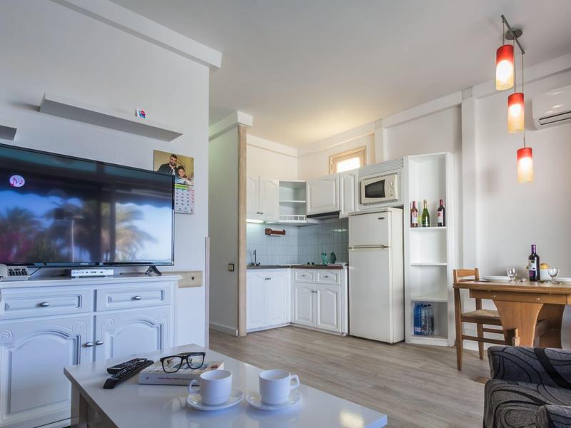 Salon moderne avec cuisine blanche, table à manger et télévision dans un appartement de vacances.