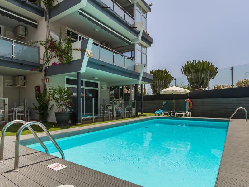 Piscine extérieure moderne à côté d'un hôtel avec plusieurs balcons et plantes.