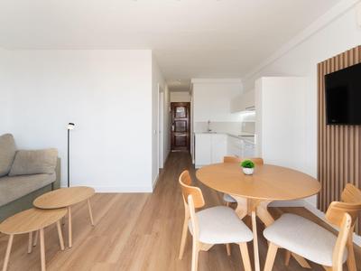 Moderner Ess- und Wohnbereich mit rundem Holztisch, Stühlen, Sofa und Fernseher an der Wand.