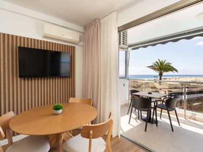 Moderner Hotelzimmerbereich mit runden Holztischen und Balkon mit Meerblick und Palmen.