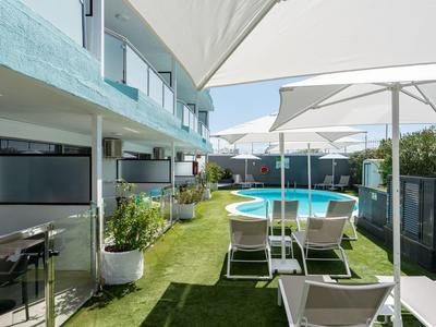 Moderner Außenbereich mit Pool, Liegestühlen und Sonnenschirmen in einer Hotelanlage.