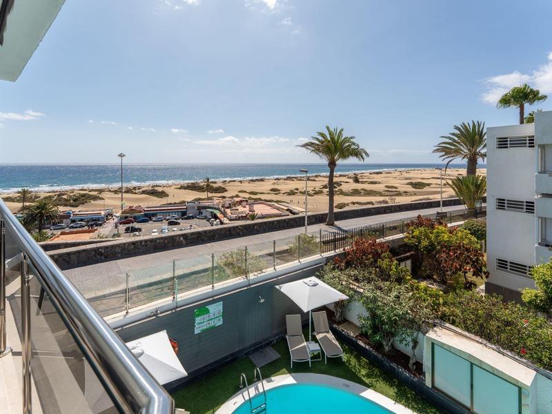 Blick vom Balkon eines Hotels auf das Meer, Palmen und einen Poolbereich.