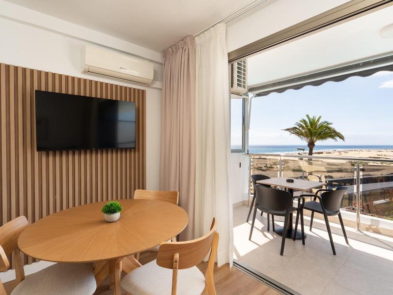 Moderner Hotelzimmerbereich mit runden Holztischen und Balkon mit Meerblick und Palmen.