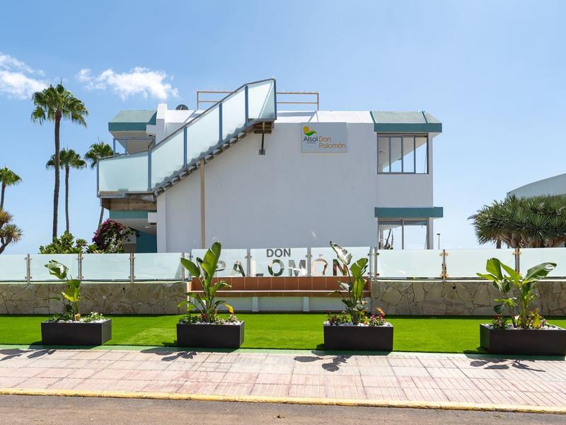 Modernes weißes Gebäude mit Außentreppe vor grünem Rasen und Palmen unter blauem Himmel