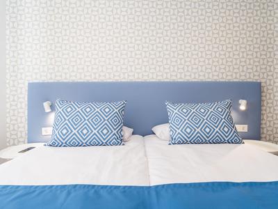 Modern double bed with blue pillows and headboard in a bright hotel room.