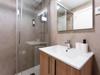 Modern bathroom with wooden vanity and glass pivot shower door.