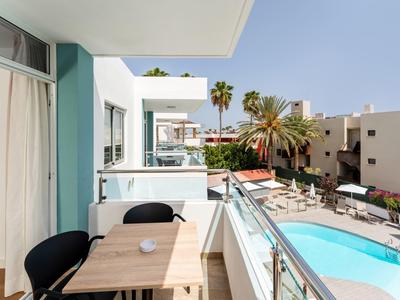 Balcony with table and chairs next to pool and modern buildings.