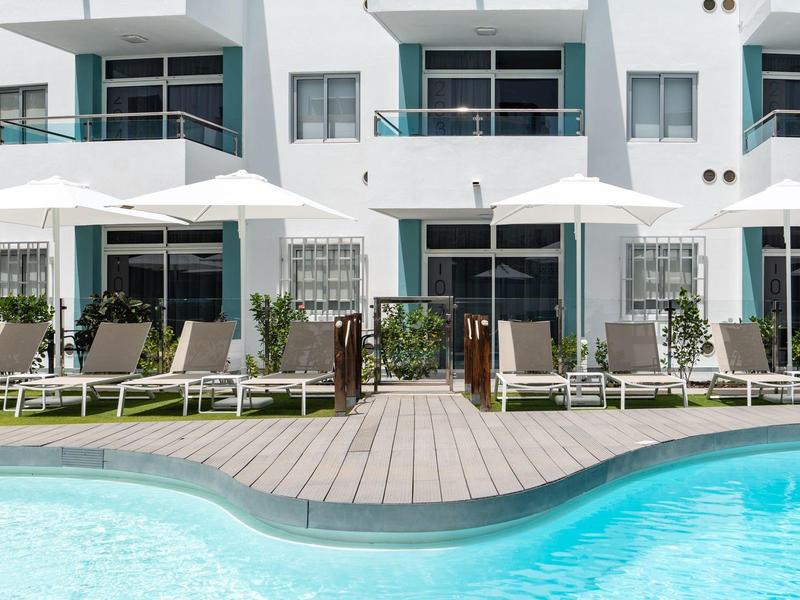 Modern outdoor pool with loungers and umbrellas in front of a white hotel building.