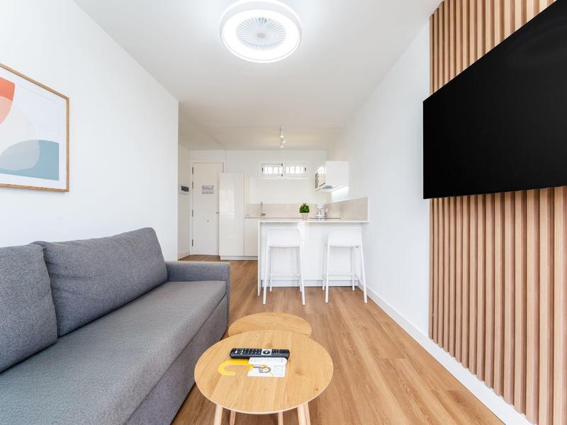 Modern living room with gray sofa, wooden table, and kitchen in the background.