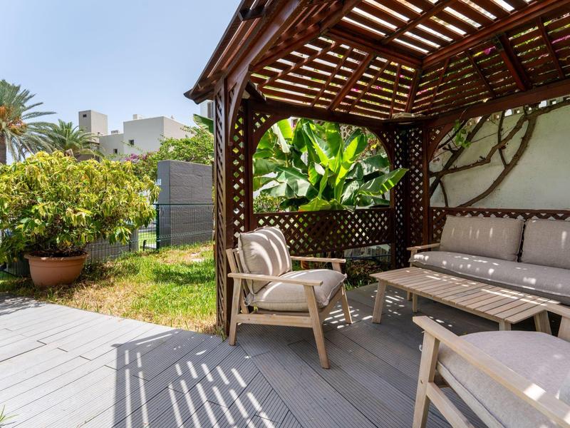 Cozy outdoor lounge under a wooden canopy with cushioned furniture in the garden.