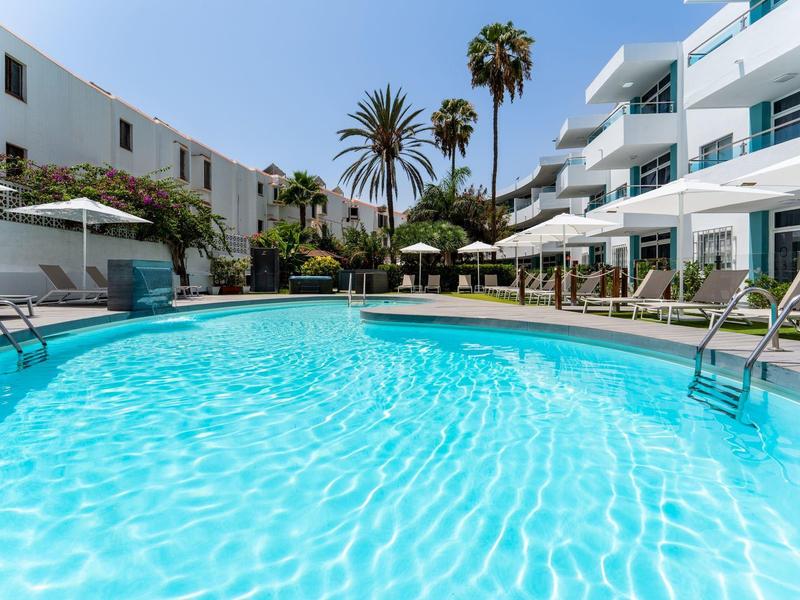 Clear outdoor swimming pool with lounge chairs and buildings on a sunny day.