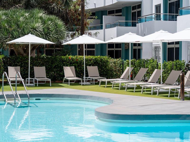 Swimming pool with lounge chairs and umbrellas next to a hotel building.