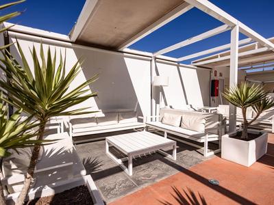 Área exterior moderna con muebles de salón blancos y plantas bajo un cielo azul.