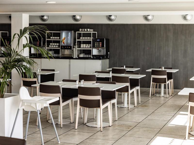 Comedor moderno con mesas blancas, sillas marrones y plantas en un restaurante de hotel.