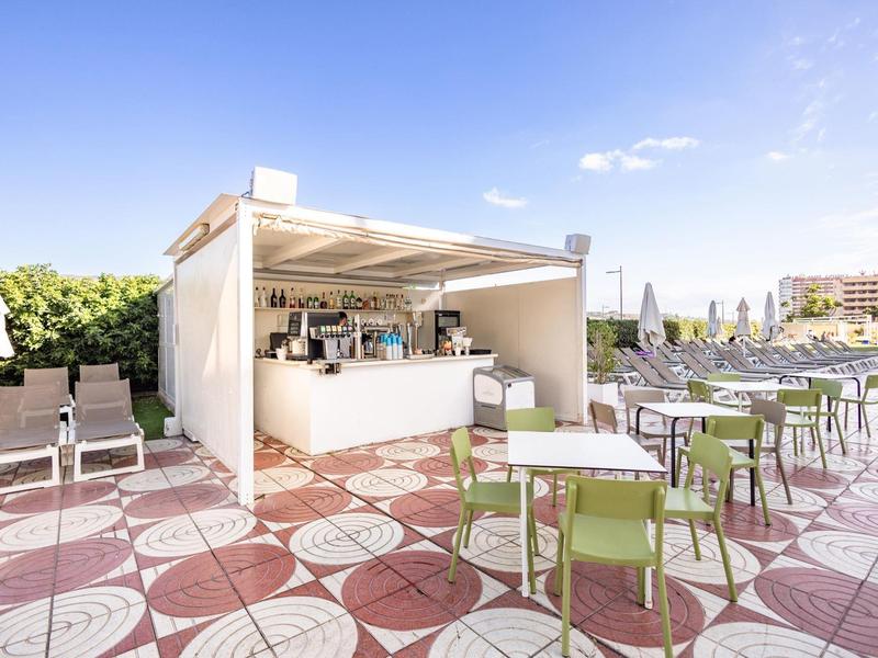 Bar al aire libre con sillas y tumbonas en una terraza bajo cielo azul.