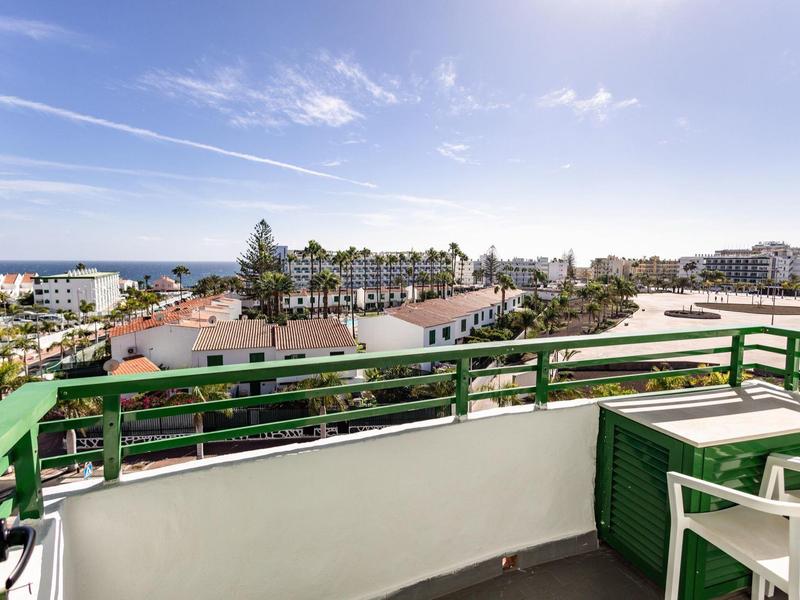 Balcón con barandilla verde, vista de edificios de la ciudad y el mar bajo cielo azul.