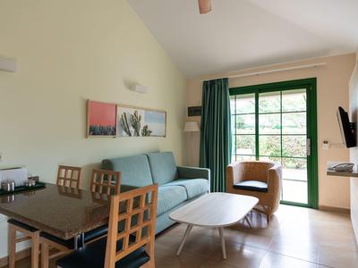 Salon confortable avec canapé, fauteuil, table à manger et grande fenêtre verte.